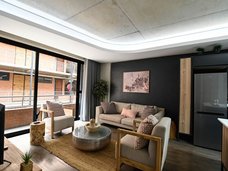 Modern open-plan living area featuring an exposed concrete ceiling with cove lighting, sleek kitchen cabinetry, and large sliding doors leading to a balcony.