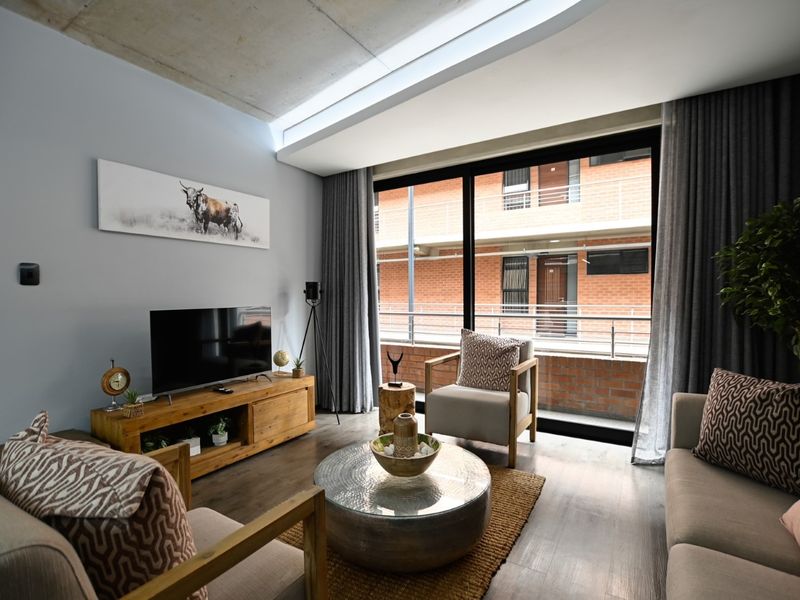 Modern living room featuring an exposed concrete ceiling, large sliding glass doors leading to a balcony, and high-quality laminate flooring.