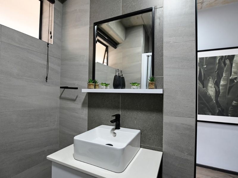 Modern bathroom featuring a contemporary vessel sink, black fixtures, a framed mirror, and sleek grey porcelain wall tiling.