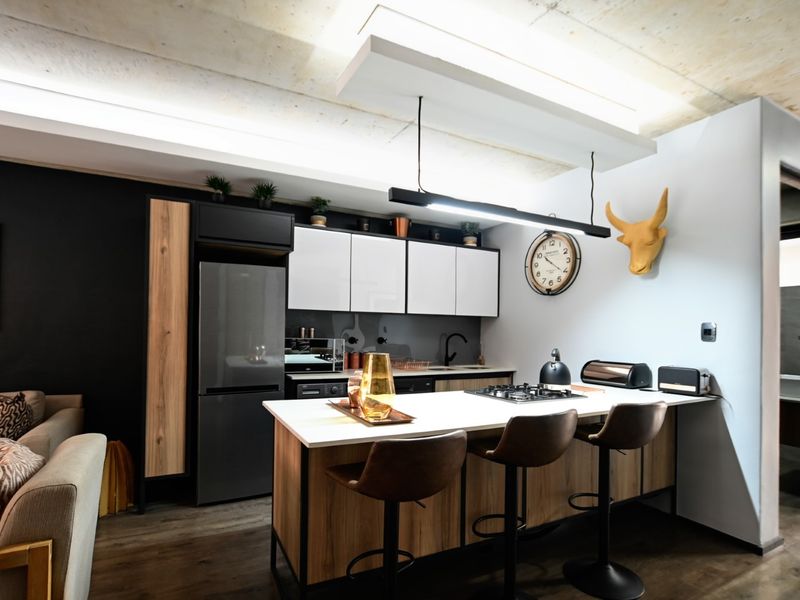 Modern open-plan kitchen featuring a central island with a gas hob, sleek cabinetry, and exposed concrete ceilings, seamlessly integrated with the living area.