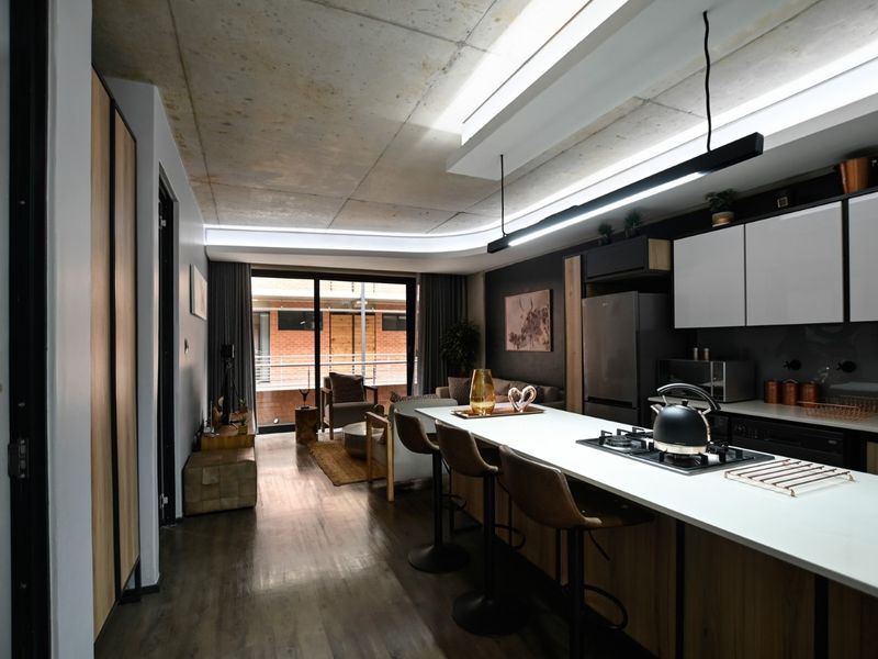 Modern open-plan apartment featuring an exposed concrete ceiling, sleek kitchen cabinetry with a central island, and seamless flow to a private balcony.