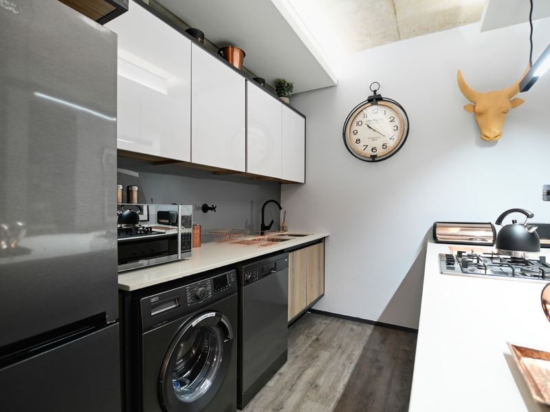 Modern kitchen featuring sleek white cabinetry, stone countertops, integrated gas hob, and high-quality finishes with wood-look laminate flooring.
