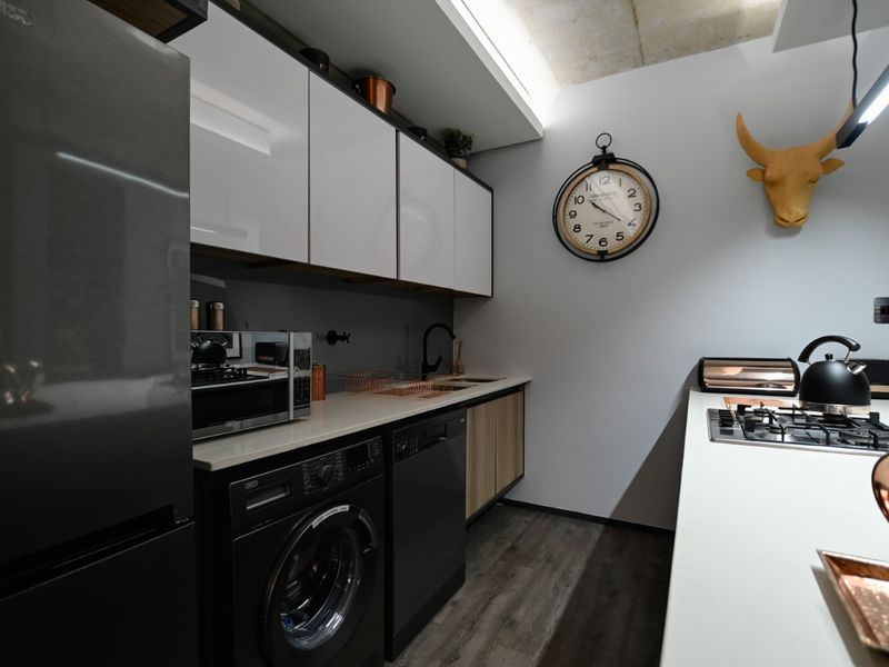 Modern kitchen featuring sleek white cabinetry, stone countertops, integrated appliances, gas cooktop, and an industrial-style exposed concrete ceiling.