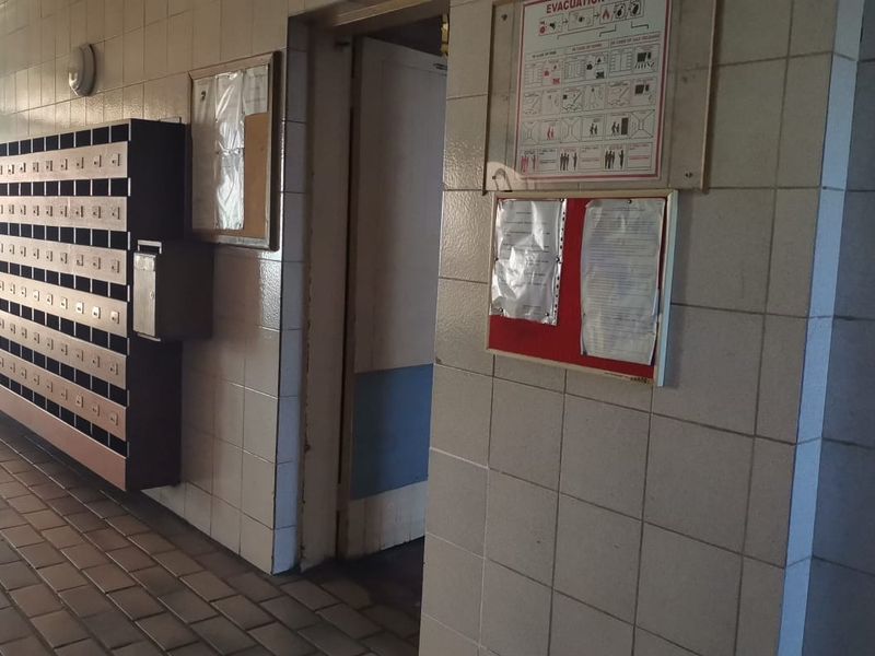 A communal apartment building hallway featuring tiled walls, tiled flooring, and a bank of built-in mailboxes for residents.