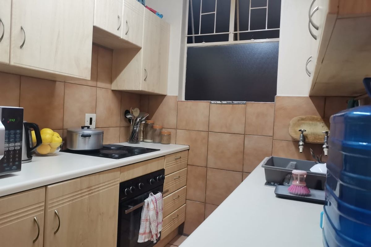 A functional kitchen featuring light wood-finish cabinetry, tiled splashbacks, an integrated electric hob and oven, and a window with security bars.