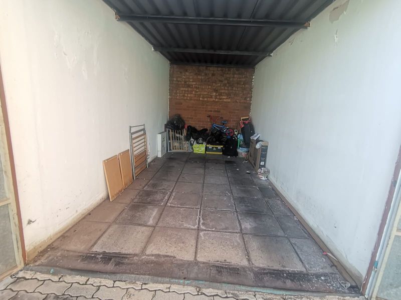 A single garage space featuring exposed brickwork, tiled flooring, and a metal roof structure, currently used for storage.