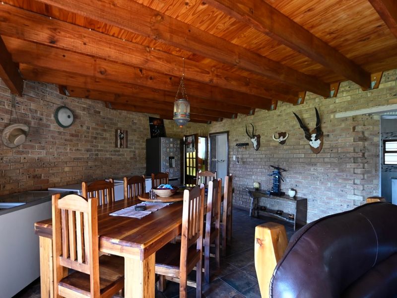 Open-plan living and dining area featuring rustic facebrick walls, exposed timber beam ceilings, and durable tiled flooring.