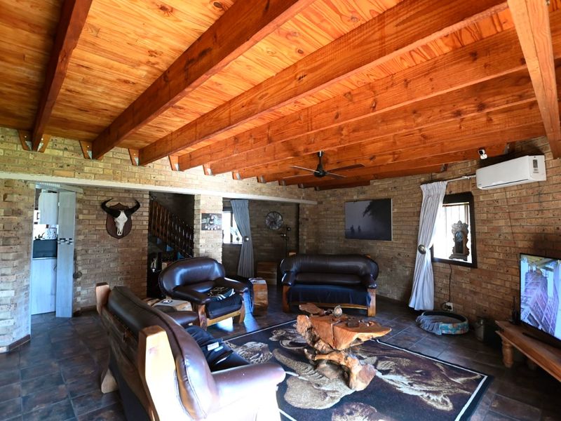 Spacious living room featuring rustic facebrick walls, exposed timber beam ceilings, tiled flooring, and a wall-mounted air conditioning unit.