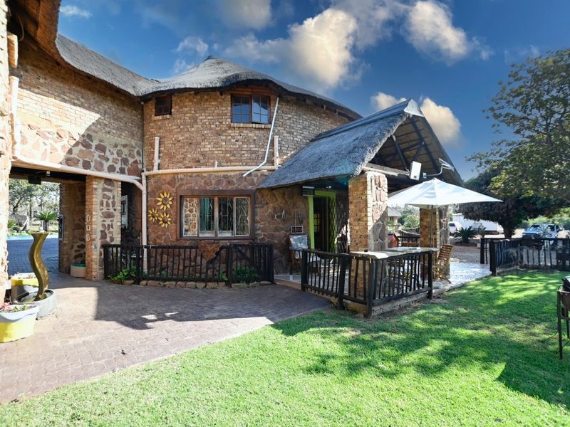 Rear view of a rustic small holding featuring a thatched roof, stone and brick facade, and a covered patio area overlooking the garden.