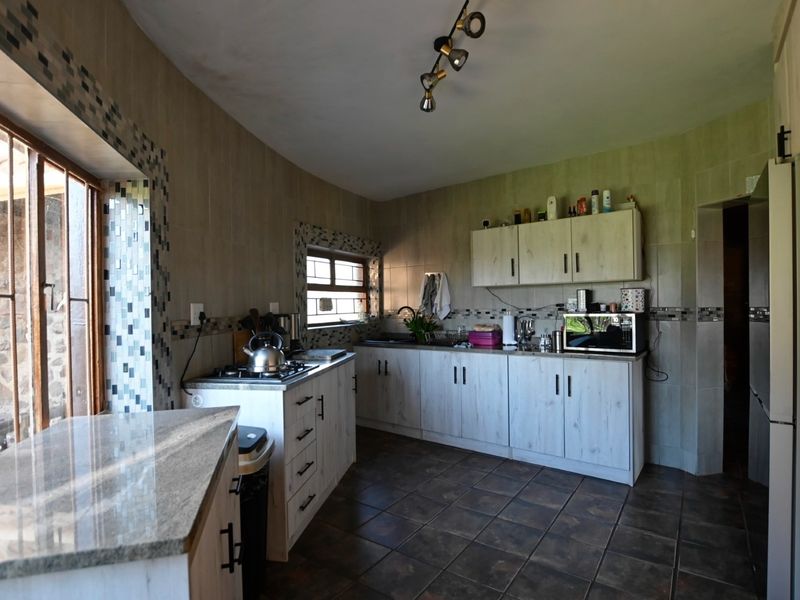 A functional kitchen featuring light wood-grain cabinetry, granite countertops, a gas hob, and decorative mosaic tile accents with tiled flooring throughout.