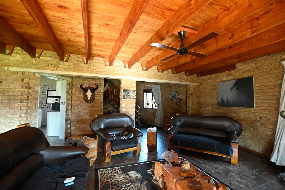 Rustic living room featuring exposed timber beam ceilings, facebrick walls, and tiled flooring, with an open flow to the staircase and adjacent areas.