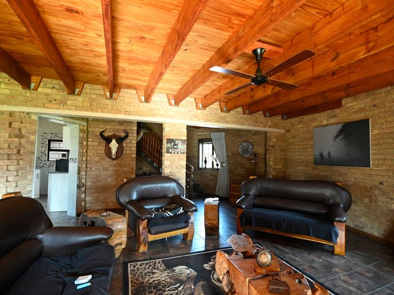 Rustic living room featuring exposed timber beam ceilings, facebrick walls, and tiled flooring, with an open flow to the staircase and adjacent areas.