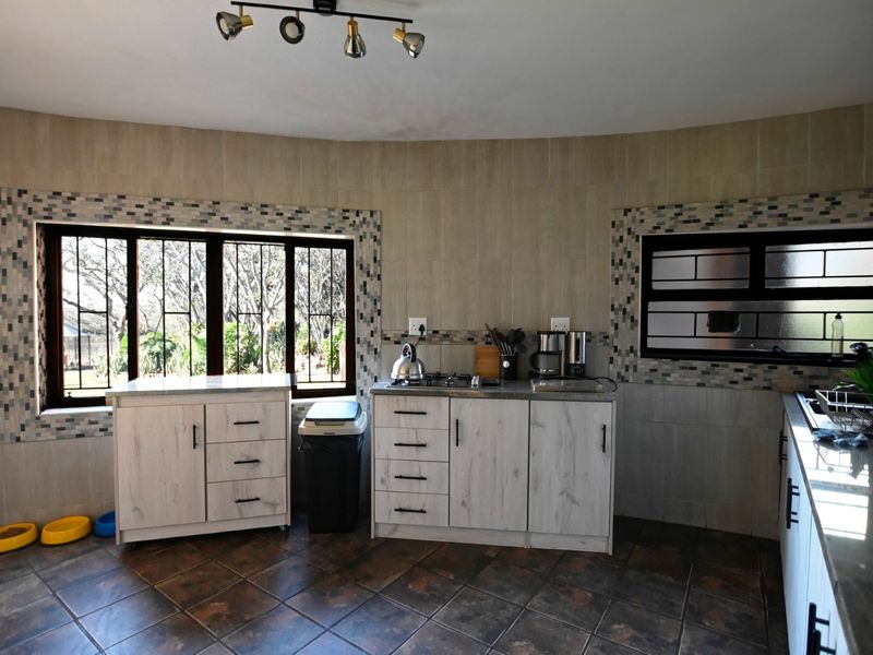 A functional kitchen featuring light wood-finish cabinetry, gas hob, tiled flooring, and decorative mosaic tile accents around the windows.