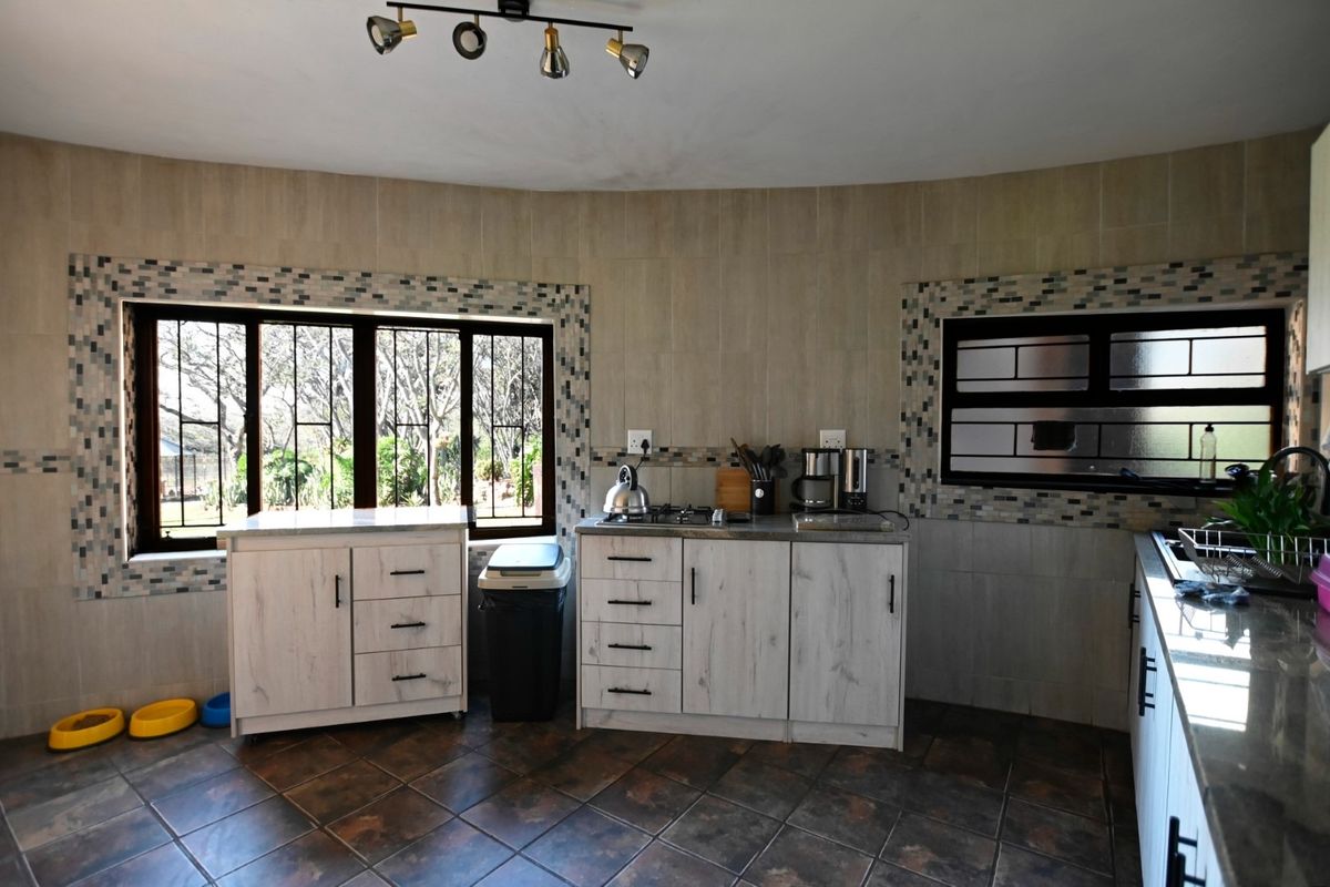 A functional kitchen featuring light wood-finish cabinetry, gas hob, tiled flooring, and decorative mosaic tile accents around the windows.