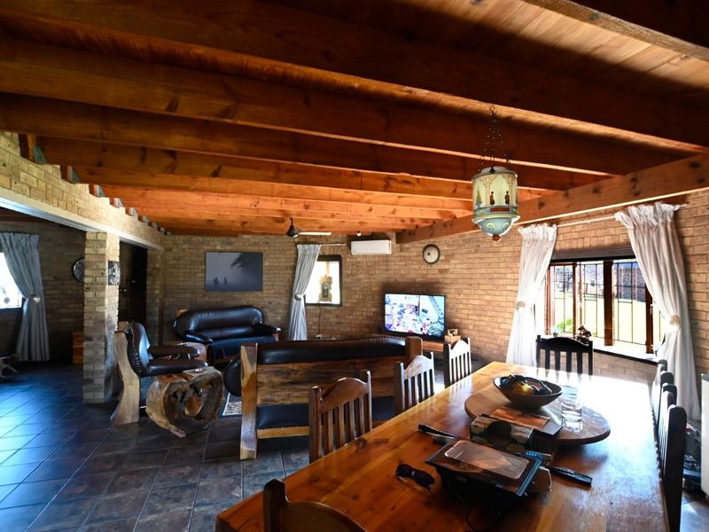 Spacious open-plan living and dining area featuring rustic facebrick walls, exposed timber beam ceilings, and tiled flooring, creating a warm and inviting atmosphere.