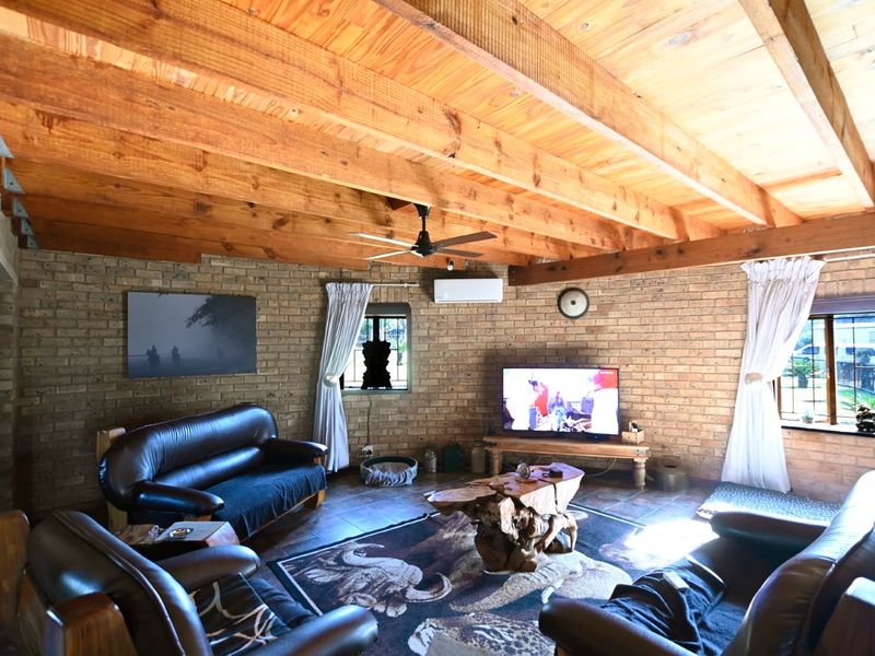 Spacious living room featuring rustic facebrick walls, exposed timber beam ceilings, and tiled flooring, creating a warm and inviting atmosphere.