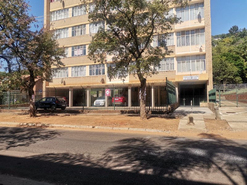 Front elevation of Tuscaloosa Flats apartment building featuring a brick facade, ground-level covered parking, and secure perimeter fencing.