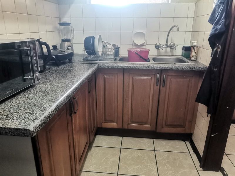 Compact kitchen featuring wooden cabinetry, granite countertops, a double basin sink, and tiled finishes throughout.