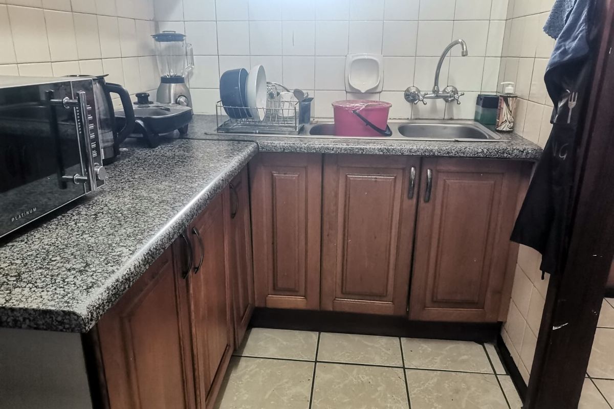 Compact kitchen featuring wooden cabinetry, granite countertops, a double basin sink, and tiled finishes throughout.
