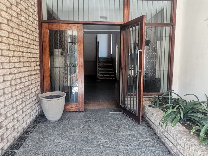 Entrance area featuring timber-framed glass doors, security gate, tiled flooring, and a brick feature wall leading to an internal staircase.