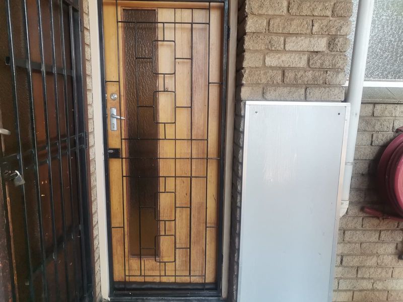 Entrance area featuring a timber door with a decorative security gate and brick exterior wall.