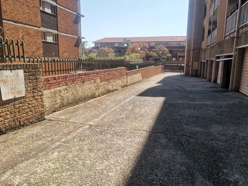 Exterior view of the apartment complex driveway featuring brick boundary walls with security fencing and access to garage units.