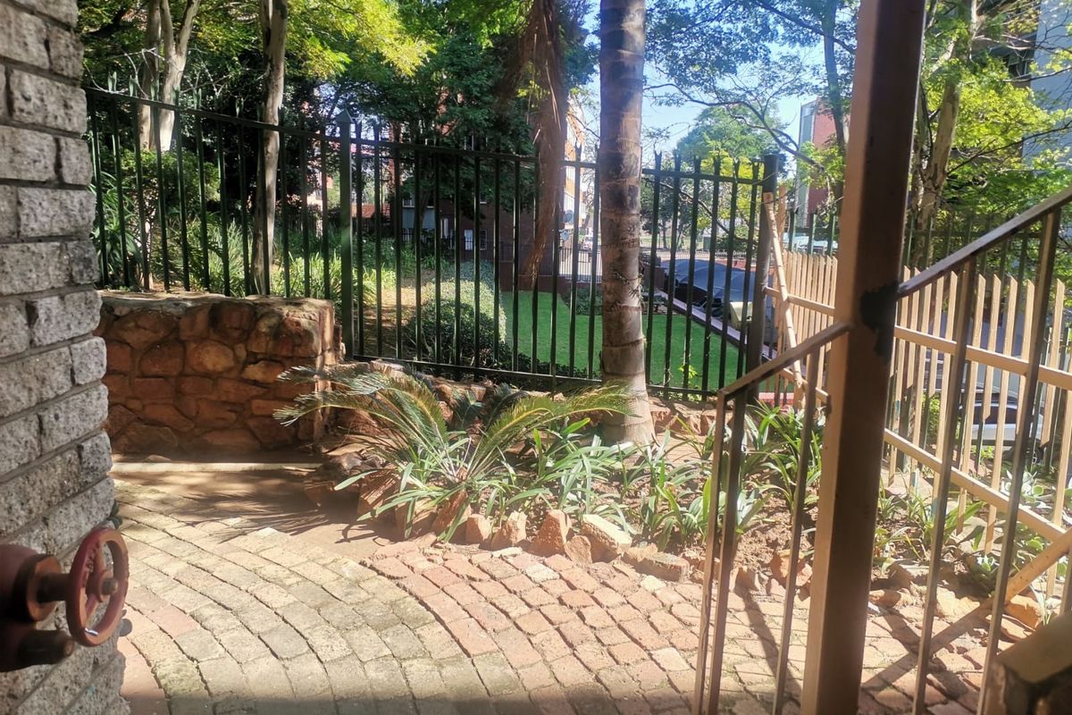 A rear outdoor area featuring brick paving, a stone retaining wall, and metal security fencing with established garden landscaping.