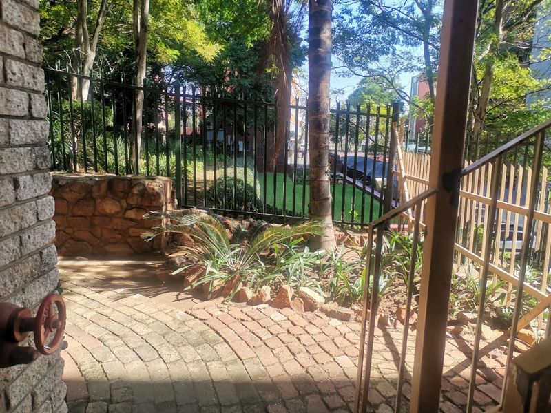 A rear outdoor area featuring brick paving, a stone retaining wall, and metal security fencing with established garden landscaping.