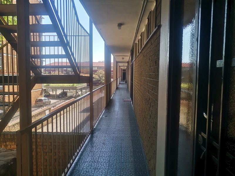 An exterior apartment walkway featuring tiled flooring, metal balustrades, and access to an external staircase.