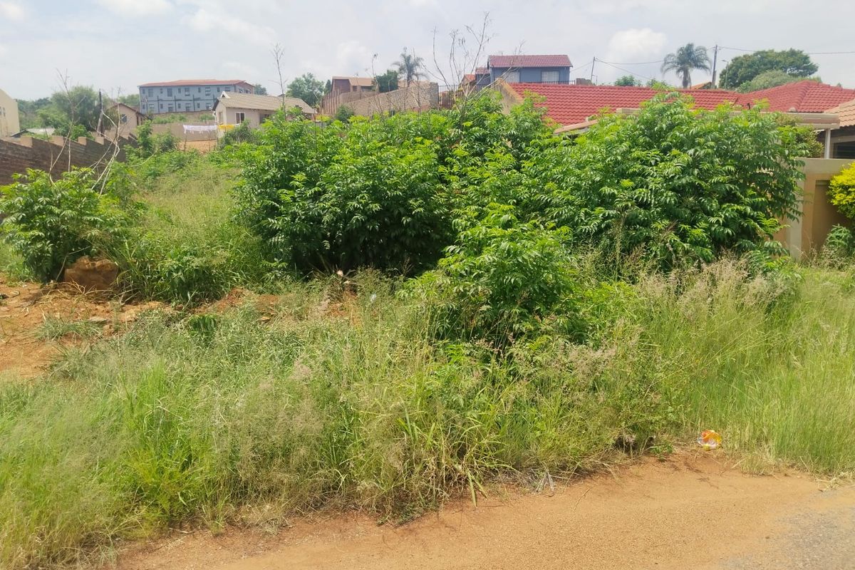A vacant residential plot featuring natural vegetation and grass, situated in an established neighborhood setting.