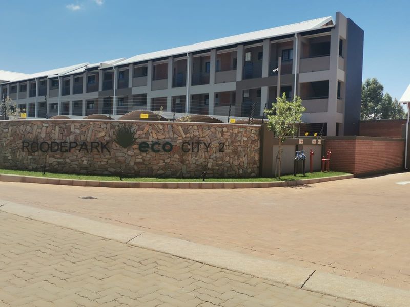 Front entrance view of Roodepark Eco City 2, featuring a stone-clad boundary wall, paved driveway, and modern multi-story apartment complex.