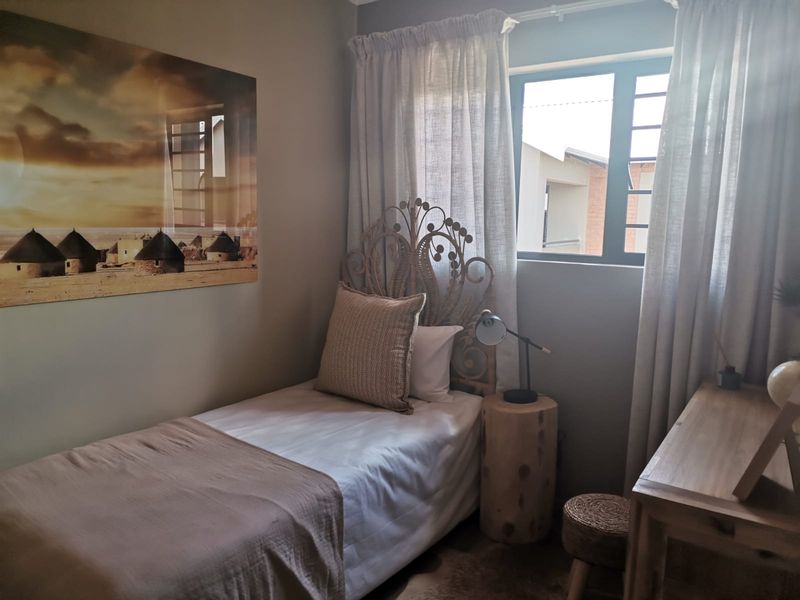 A cozy bedroom featuring neutral wall tones and an aluminium-framed window with installed curtain tracks.