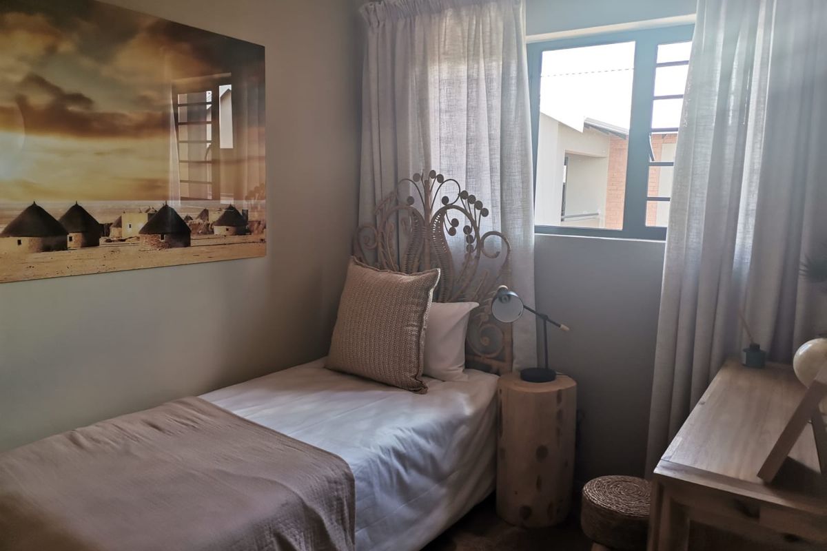 A cozy bedroom featuring neutral wall tones and an aluminium-framed window with installed curtain tracks.