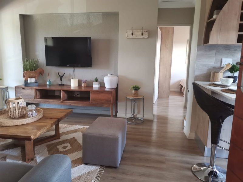 Open-plan living area featuring modern laminate flooring, a recessed wall niche for media, and a functional kitchen with stone countertops.