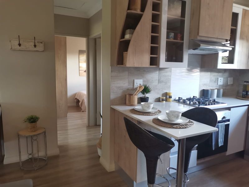Modern kitchen featuring light wood cabinetry, a gas hob with extractor, tiled backsplash, and an integrated breakfast bar, leading into a hallway.