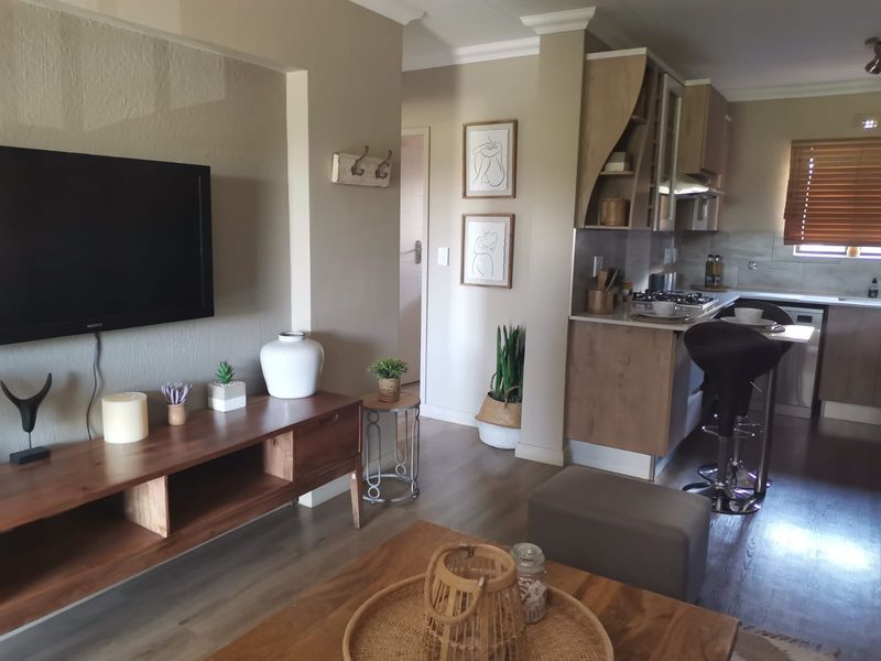 An open-plan living and kitchen area featuring modern wood-tone cabinetry, laminate flooring, and a functional layout with integrated kitchen appliances.