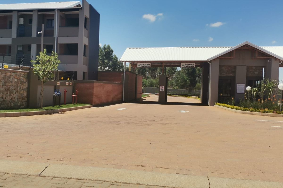 The main entrance to the apartment complex featuring a secure gatehouse, paved driveway, and modern architectural finishes.