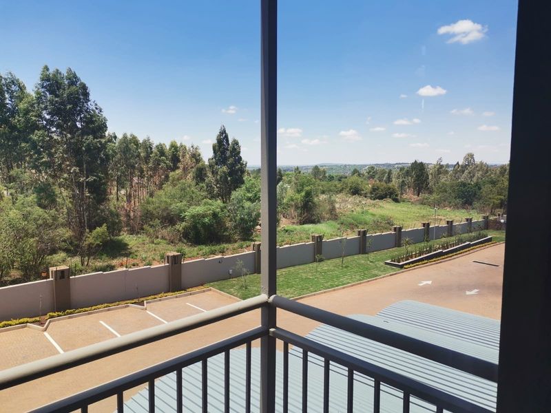 A balcony overlooking a paved parking area, perimeter wall, and surrounding landscape.