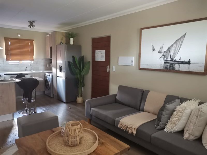 Open-plan living area featuring a modern kitchen with integrated appliances, laminate flooring, and neutral wall finishes, creating a cohesive and functional living space.