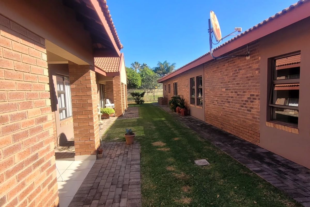 A view of the rear exterior area featuring a paved walkway between two face brick buildings with a central lawn and tiled roofing.
