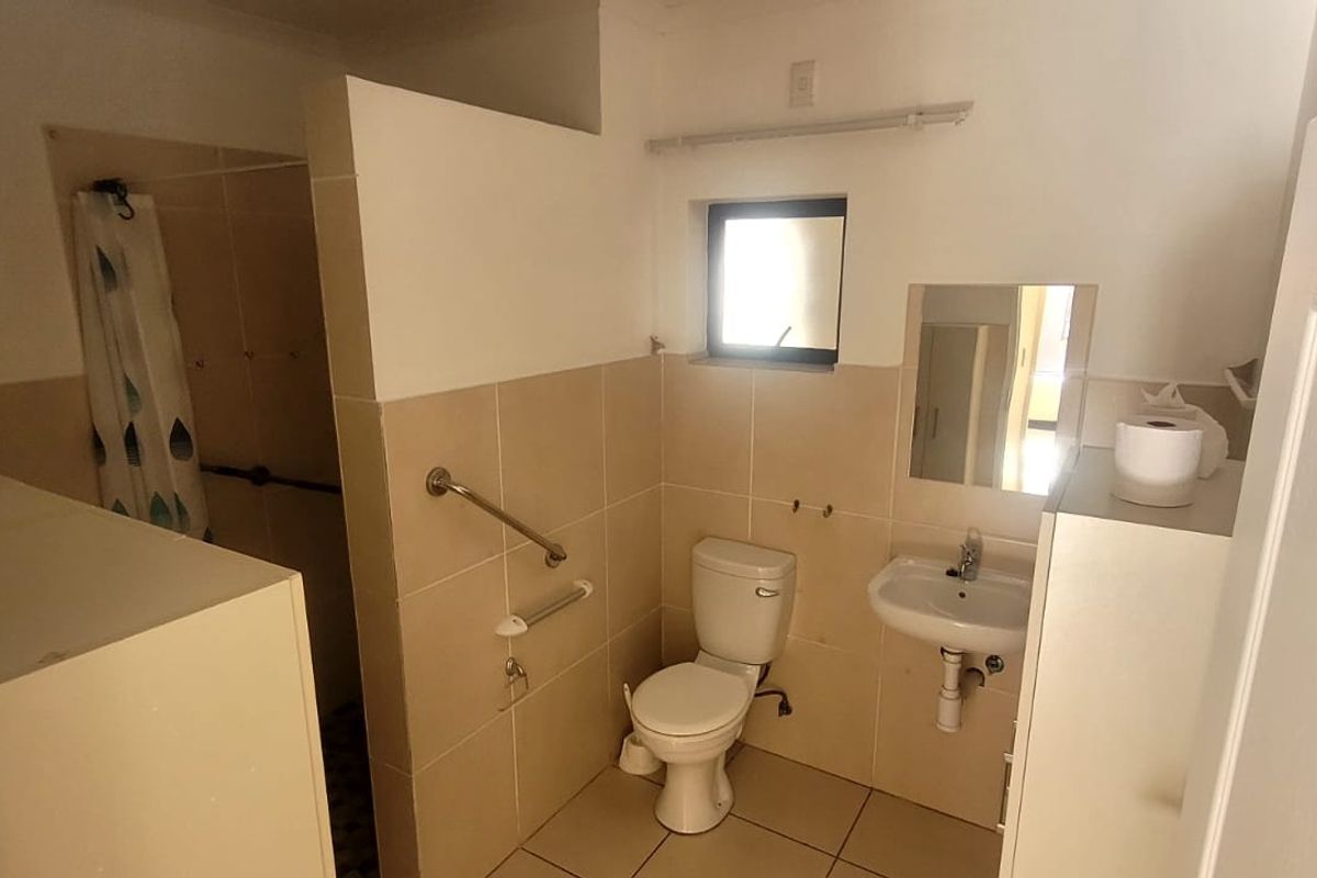 Functional bathroom featuring a toilet, pedestal washbasin, and a shower enclosure with safety grab rails installed for accessibility.