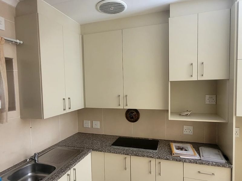 A functional kitchen featuring neutral built-in cabinetry, granite countertops, a stainless steel sink, and an integrated electric hob with tiled backsplash.