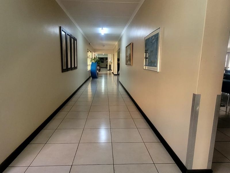A long, well-lit hallway featuring neutral walls, tiled flooring, and protective corner guards, providing access to adjacent communal areas.