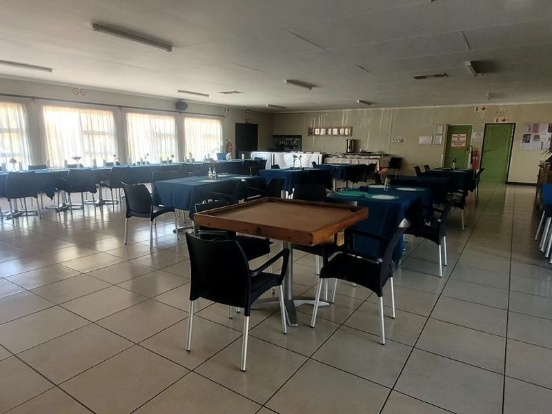 Spacious communal clubhouse area featuring tiled flooring, large windows for natural light, and functional overhead lighting, suitable for social gatherings and events.
