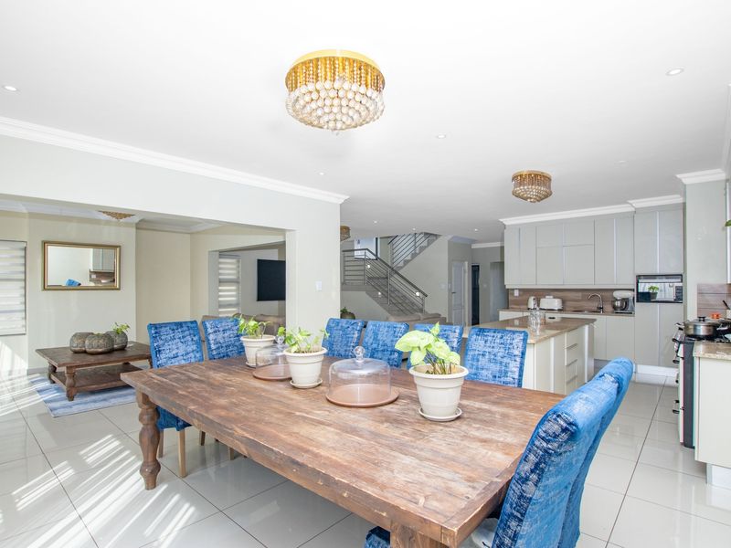 Spacious open-plan living and dining area featuring a modern kitchen with stone countertops, built-in appliances, and tiled flooring, leading to an internal staircase.