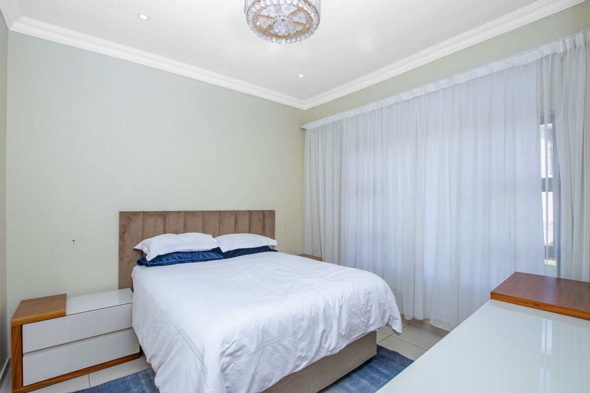 A well-maintained bedroom featuring tiled flooring, crown molding, recessed lighting, and a large sliding glass door with floor-to-ceiling curtains.