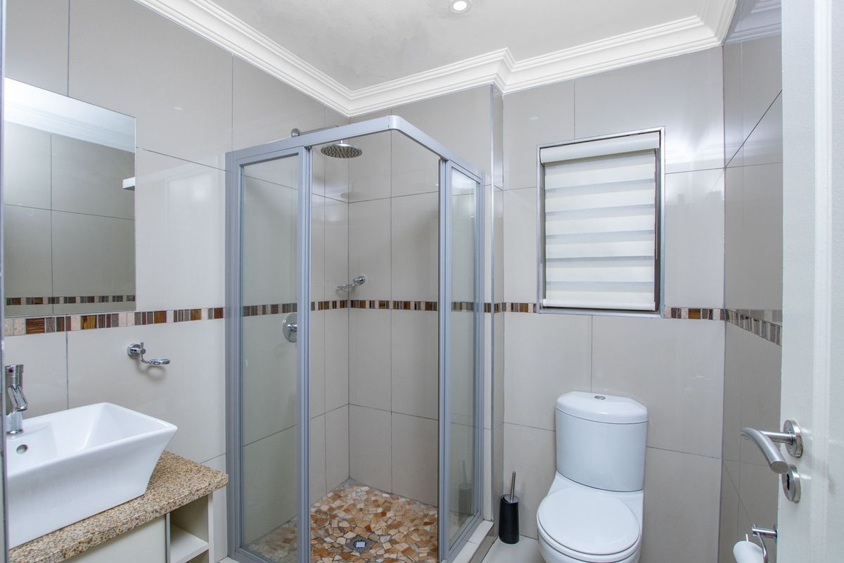 A modern, well-maintained bathroom featuring a glass shower enclosure, granite-topped vanity, and neutral wall tiling with a decorative mosaic accent.