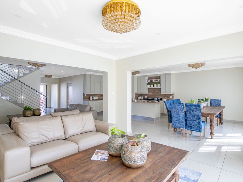 Spacious open-plan living area featuring a modern kitchen with island, tiled floors, and a staircase with a contemporary metal balustrade.