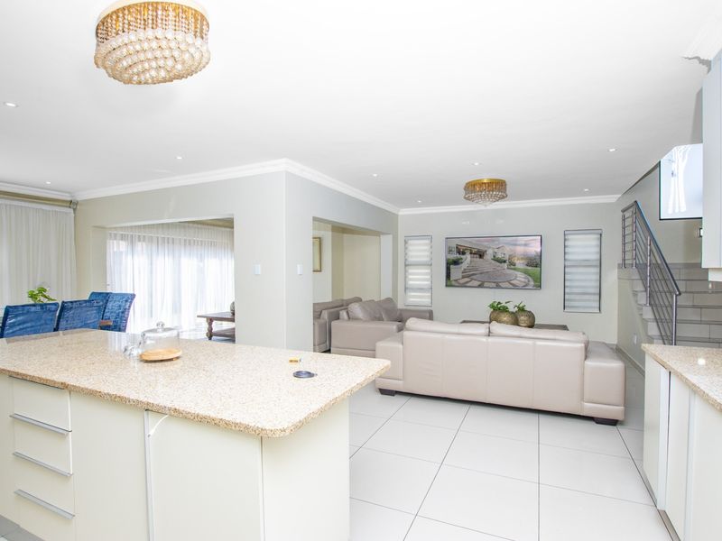 Spacious open-plan living area featuring a granite kitchen island, tiled floors, elegant crystal chandeliers, and a staircase with modern metal railings.