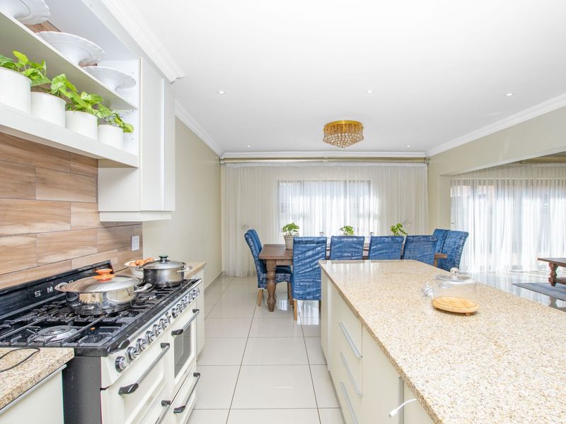 Spacious open-plan kitchen and dining area featuring a large granite island, modern gas stove, and neutral tiled flooring throughout.